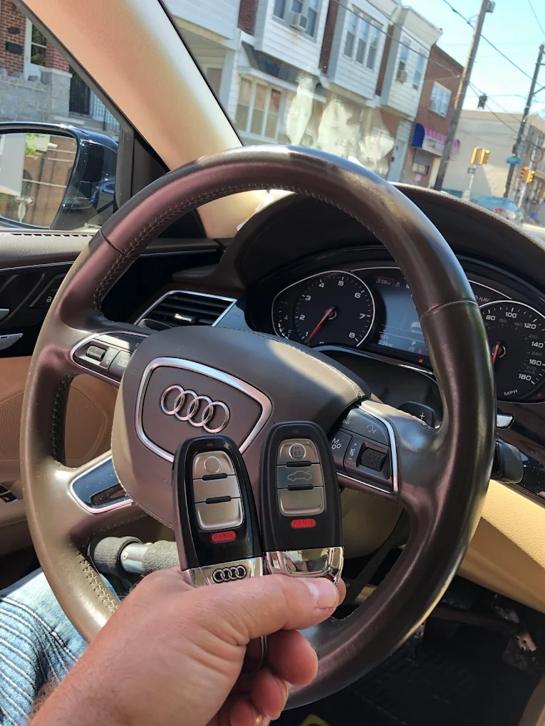 Two freshly programmed Audi smart keys held in front of an Audi Q5 steering wheel with the four-rings emblem visible