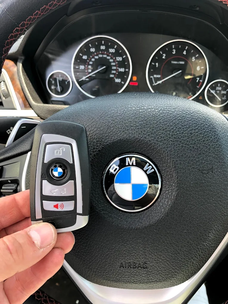 Freshly programmed BMW key fob held in front of the BMW steering wheel airbag with BMW roundel emblem and dashboard gauges visible