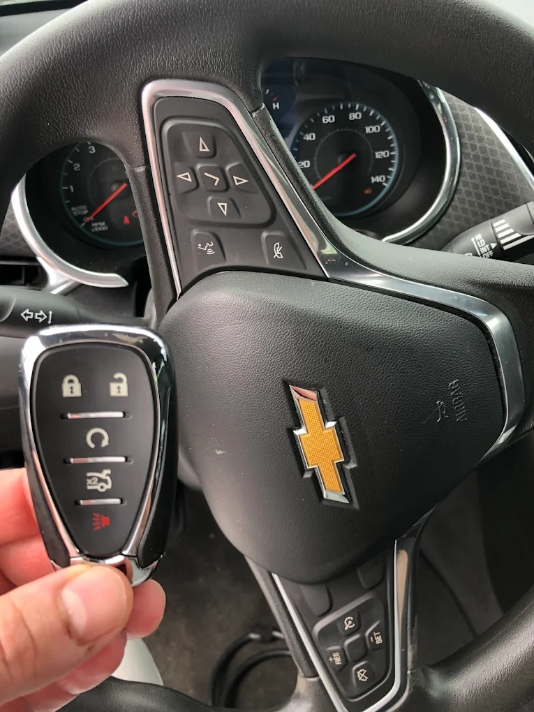 Freshly programmed Chevrolet diamond-shape smart key held in front of the Chevy gold bowtie emblem on the steering wheel airbag