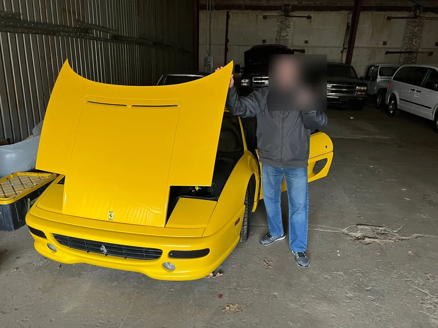 Customer holding a freshly programmed Ferrari key with prancing-horse keychain next to a bright yellow Ferrari V8 with the front clamshell hood raised in the American Best Locksmith service garage