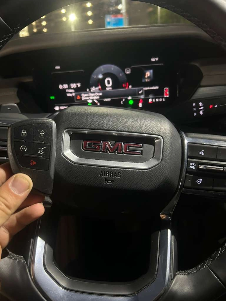 Freshly programmed 2025 GMC Acadia smart key held in front of the red GMC emblem on the steering wheel airbag with the current-generation digital instrument cluster visible behind