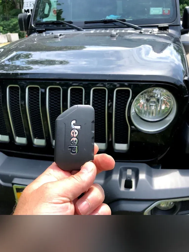 Freshly programmed Jeep Wrangler smart key held in front of a black Jeep Wrangler with the iconic 7-slot grille and round headlights clearly visible