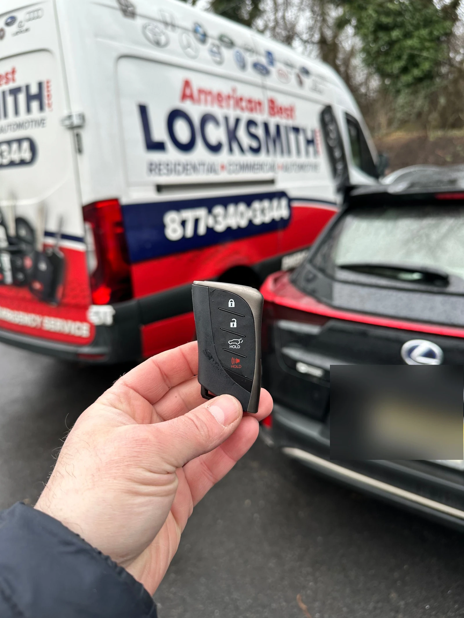 Freshly programmed Lexus smart key held in front of a red Lexus and the American Best Locksmith service van after an on-site key replacement