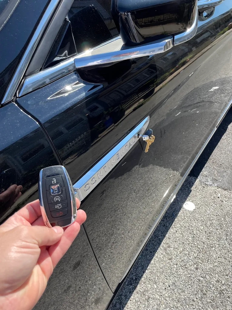 Freshly programmed Lincoln Continental smart key held in front of a black Lincoln Continental sedan with the chrome CONTINENTAL badge clearly visible on the side panel