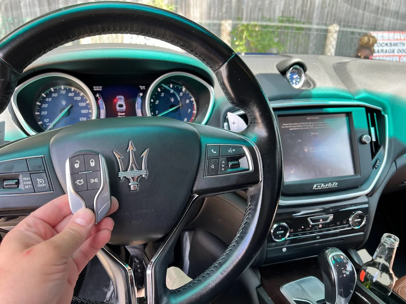 Freshly programmed Maserati Ghibli smart key held in front of the Maserati trident emblem on the steering wheel airbag with the GHIBLI badge visible on the dashboard infotainment screen