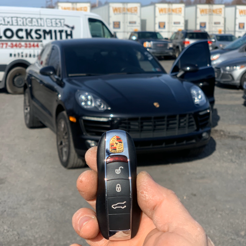 Freshly programmed Porsche Macan key fob held in front of a black Porsche Macan with the American Best Locksmith service van visible in the background