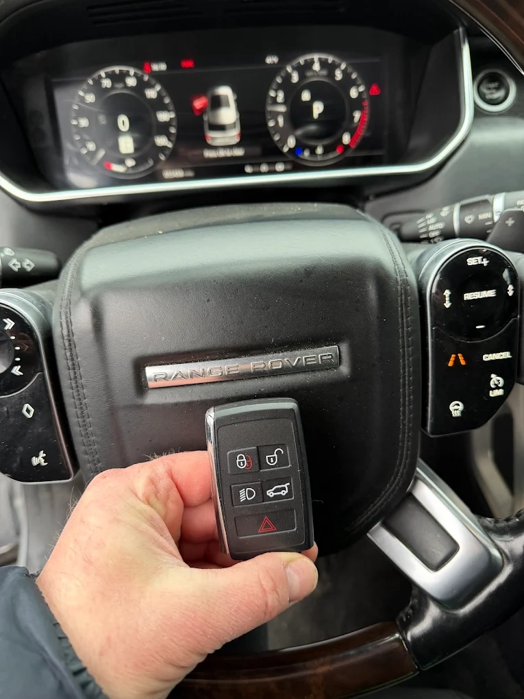Freshly programmed Range Rover smart key fob held in front of the iconic embossed RANGE ROVER badge on the steering wheel airbag