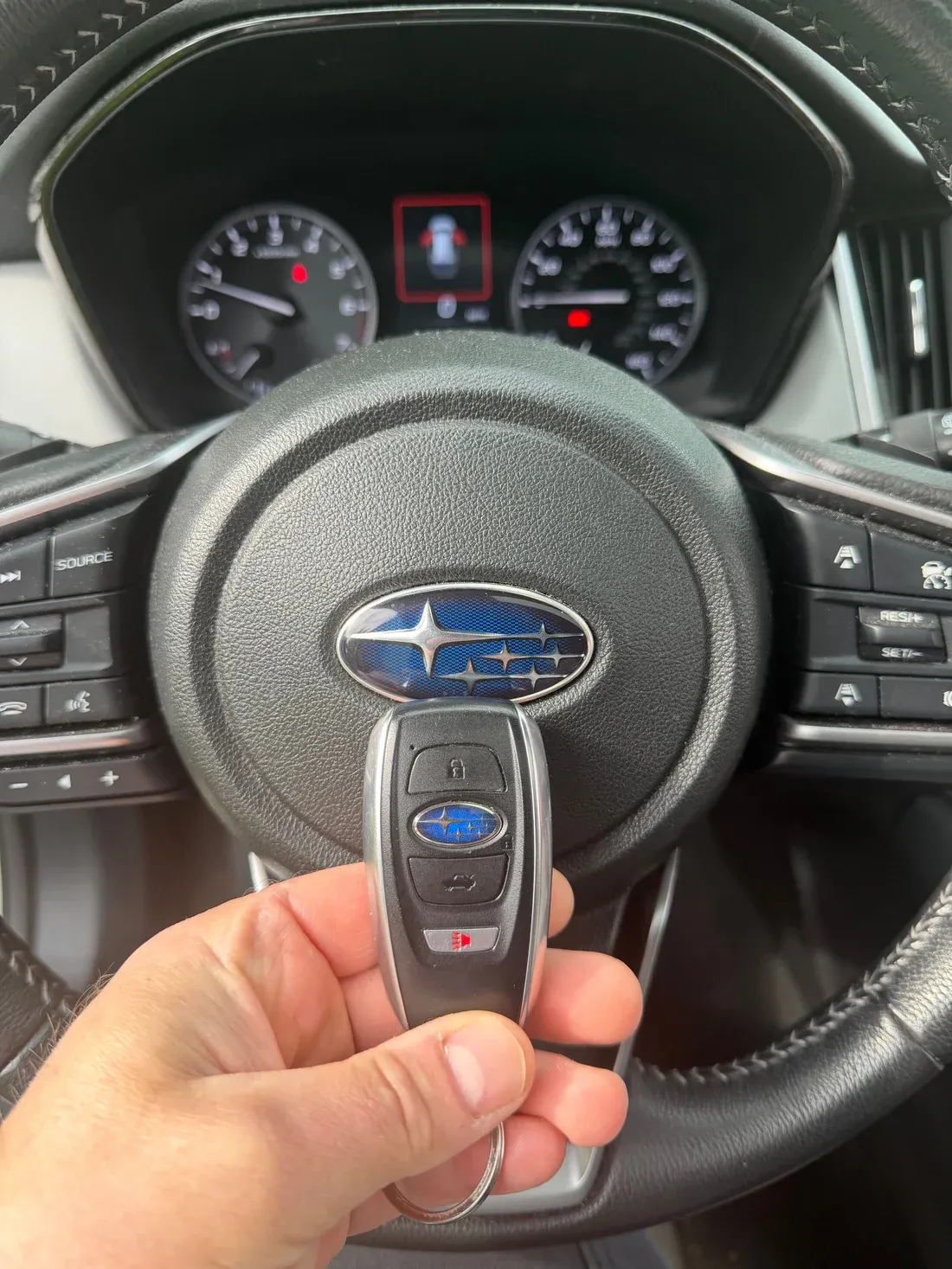 Freshly programmed 2025 Subaru Outback 4-button smart key held in front of the steering wheel with the blue Subaru star-cluster emblem and instrument cluster visible behind