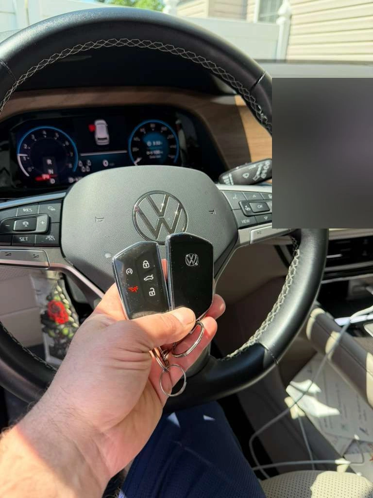 Pair of freshly programmed Volkswagen Atlas keys (smart key + remote) held in front of the VW emblem on the steering wheel with the digital instrument cluster visible
